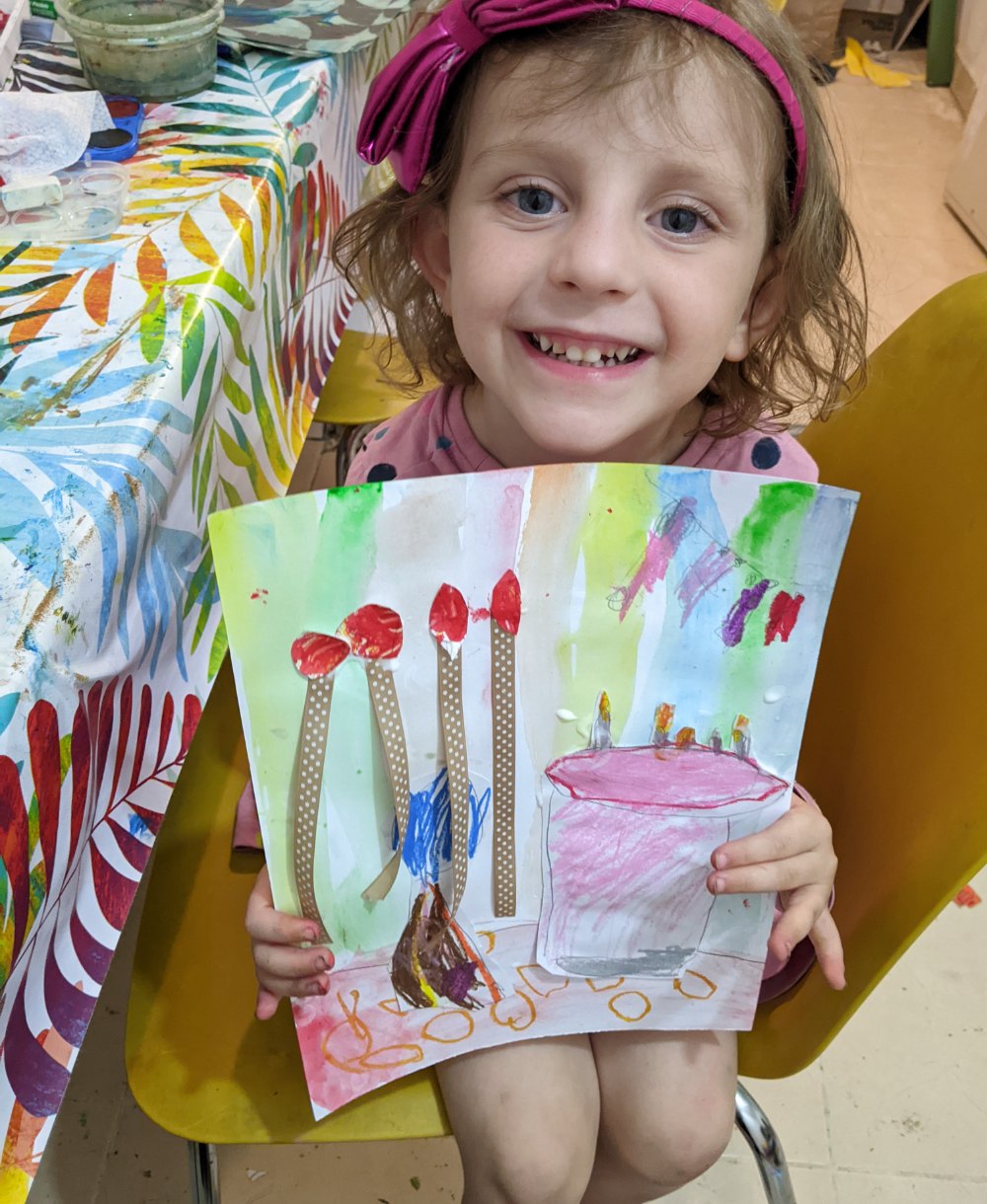 A proud young girl holding up her colourful painting