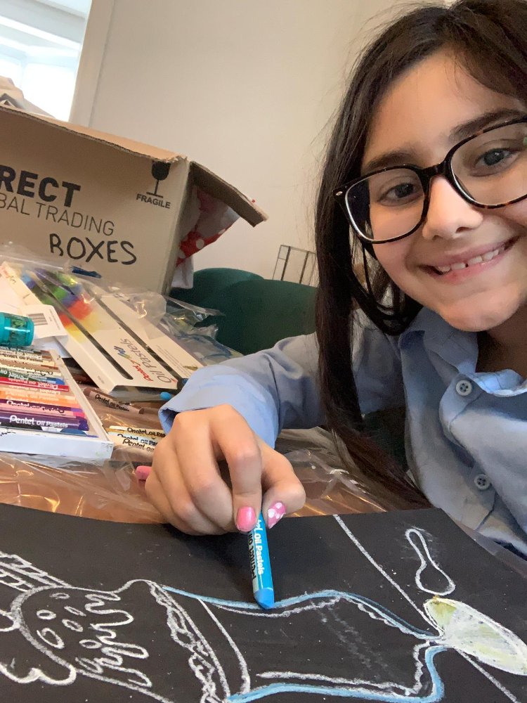 A girl with oil pastels working on a black-paper drawing