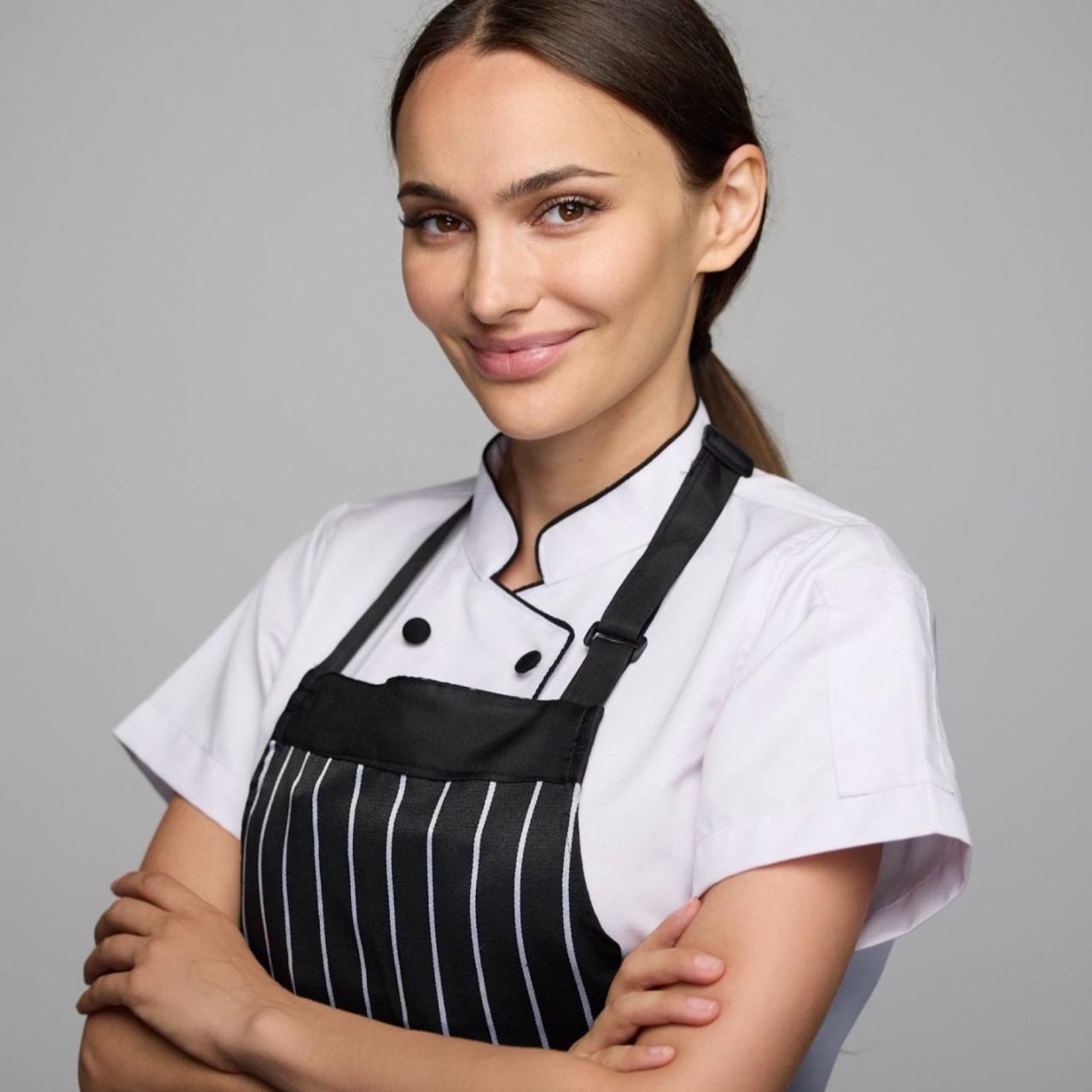 Natalie Golba in a chef's apron, smiling, arms crossed in a bright kitchen