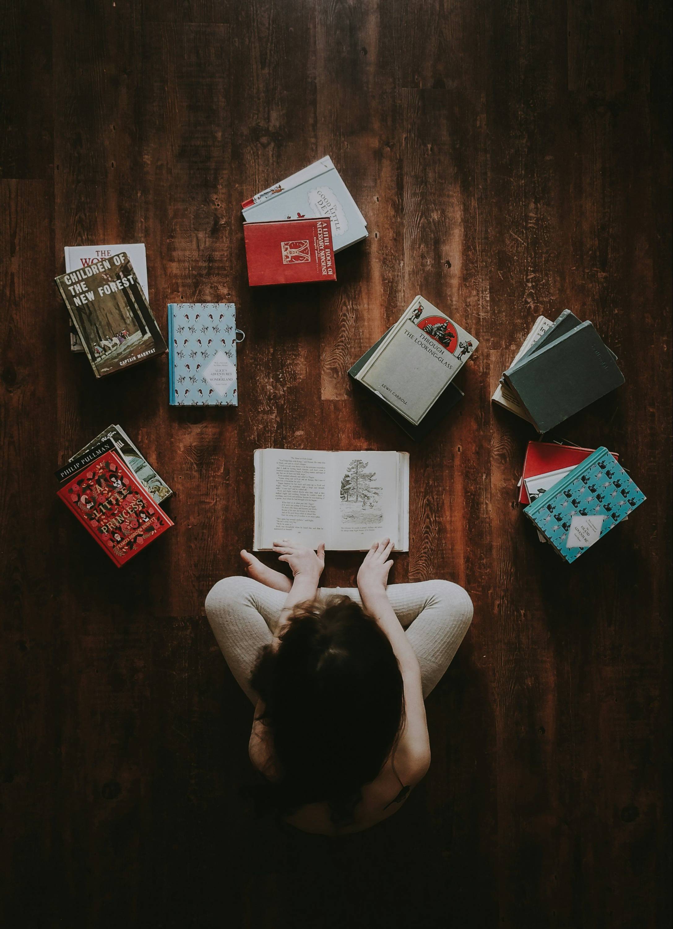 A school-age child sitting on the floor reading a book, with a circle of other books spread out around them.
