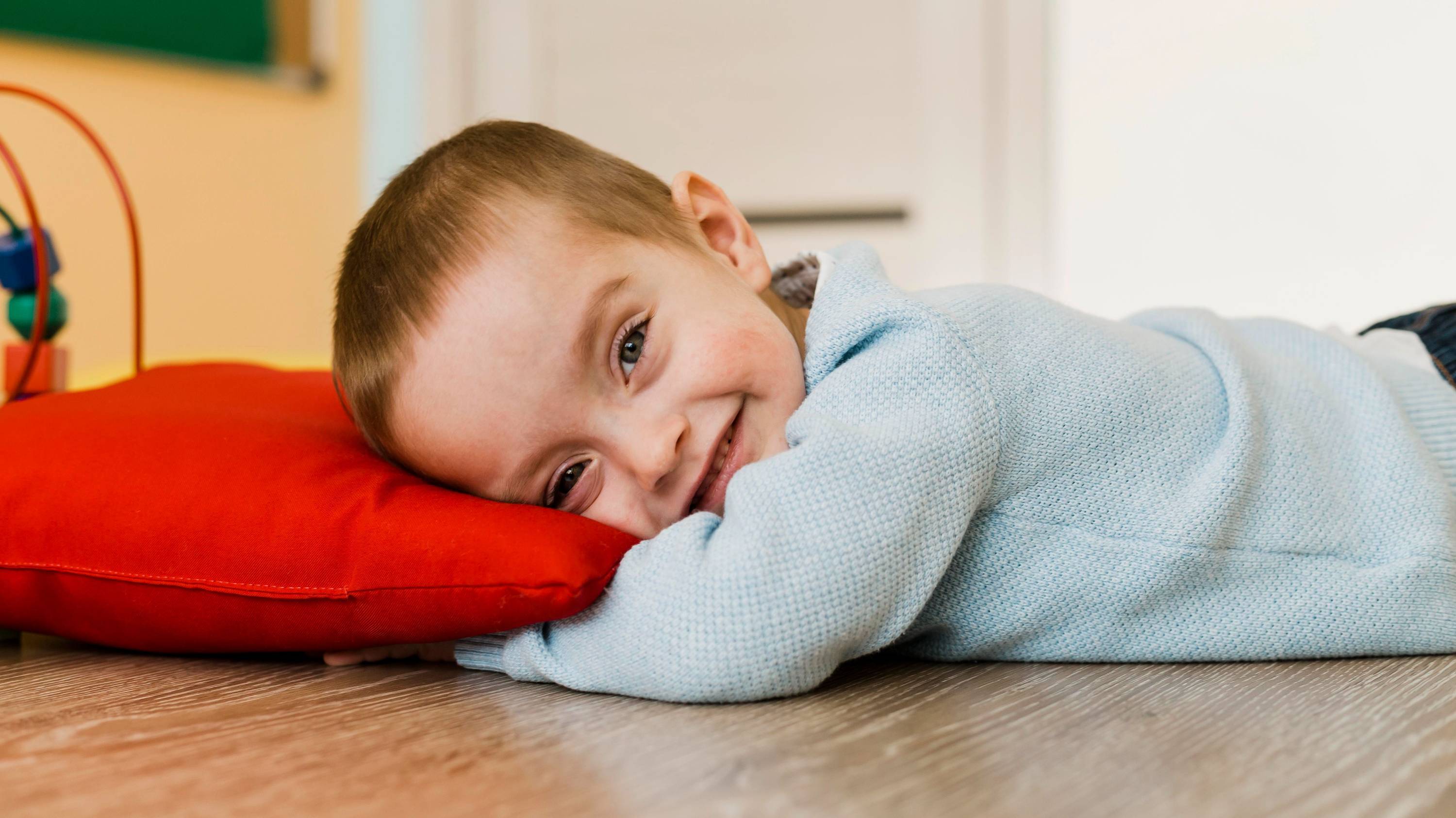 A young child lying on a red cushion on the floor, resting during quiet time.