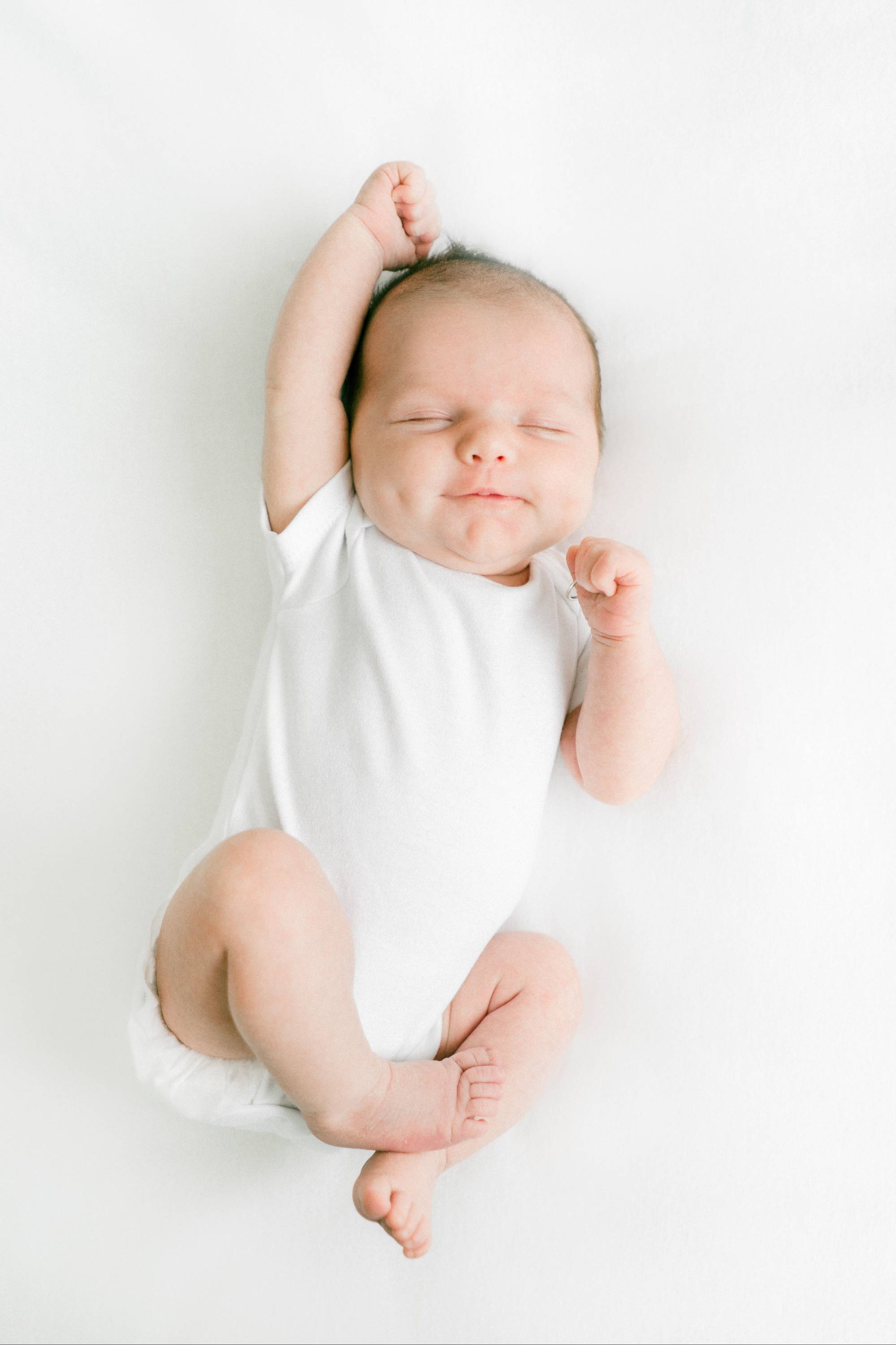A baby sleeping on their back on a firm, flat surface with a fitted sheet and nothing else around them