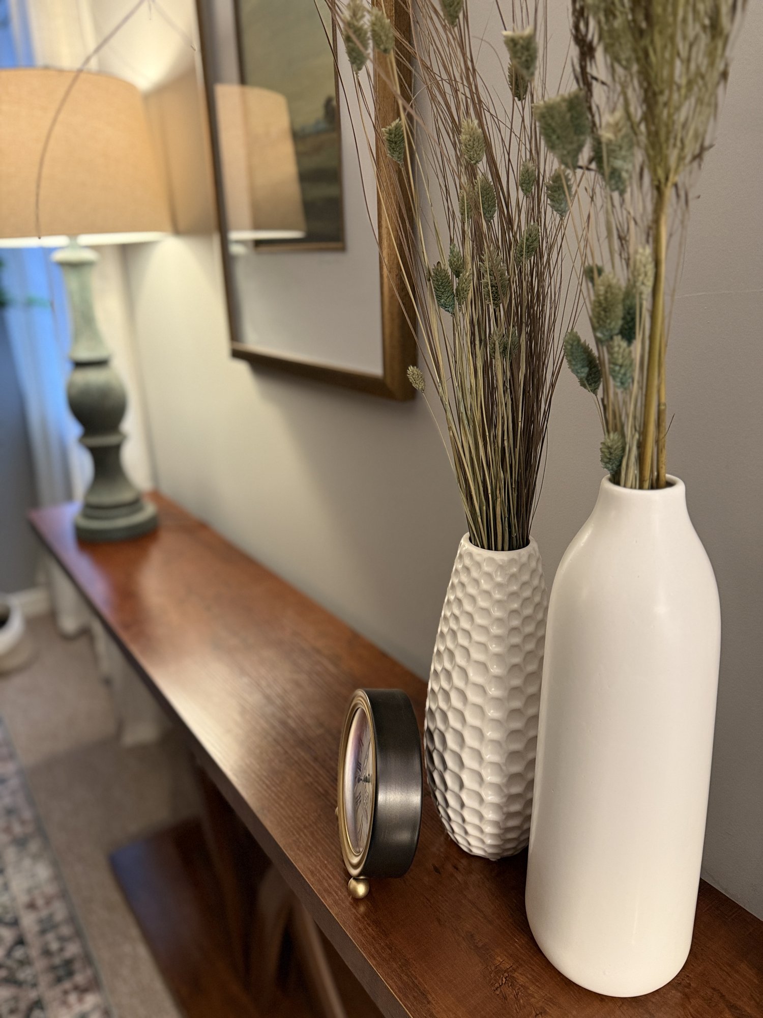 A wooden console with white vases, dried grasses, and a small clock in Kristen's office