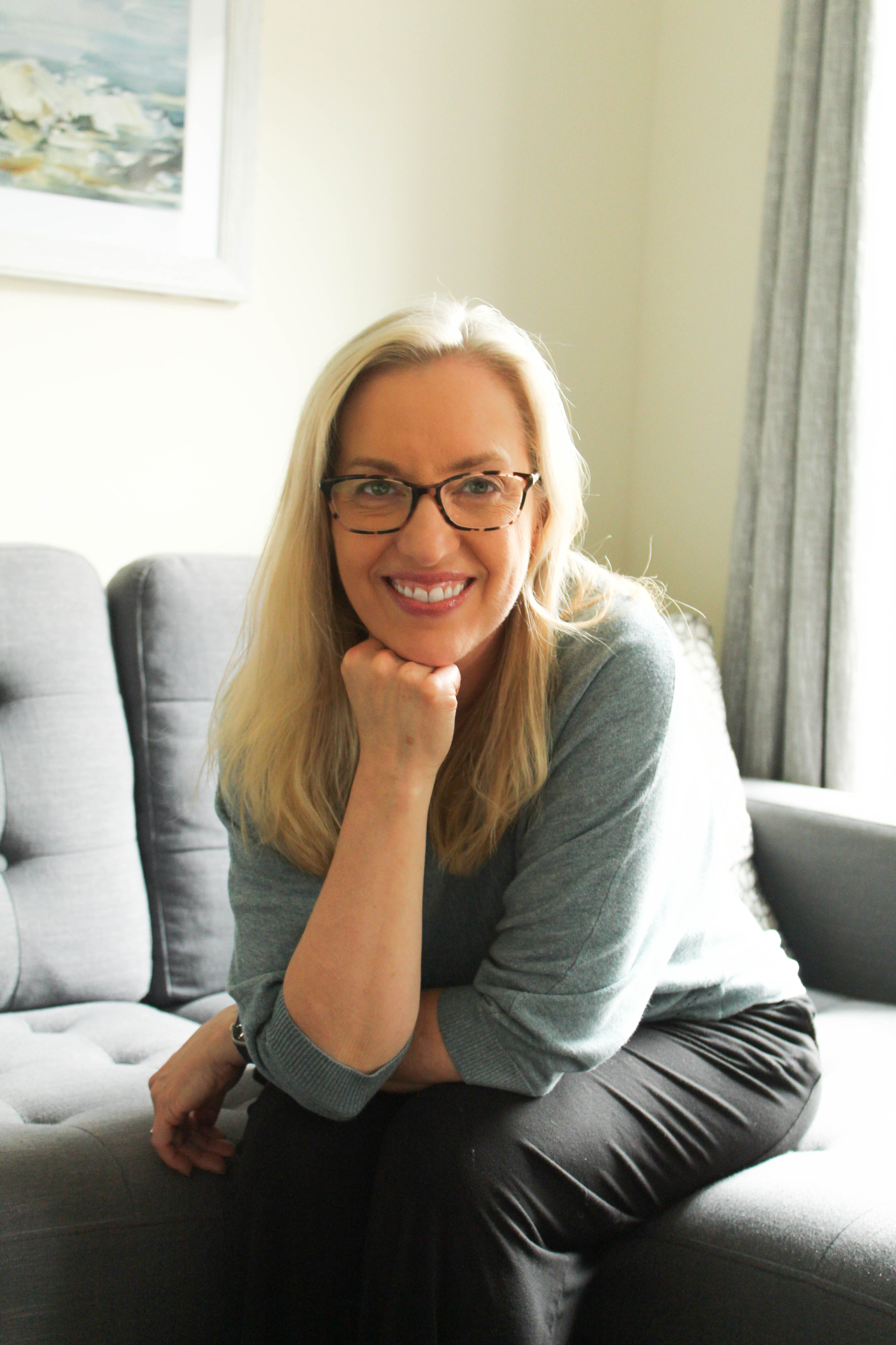 Kristen K. Wold sitting on a couch, chin resting on her hand, smiling