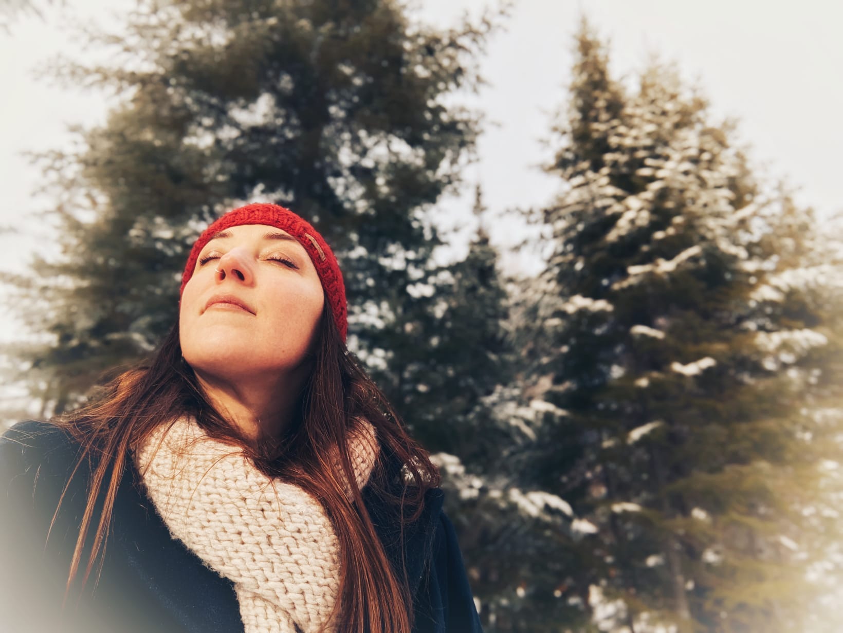 Marilyn outdoors in winter, eyes closed and face lifted toward the sky beneath snow-dusted pines