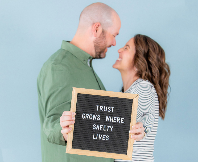 David and Carrie holding a sign saying Trust Grows Where Safety Lives