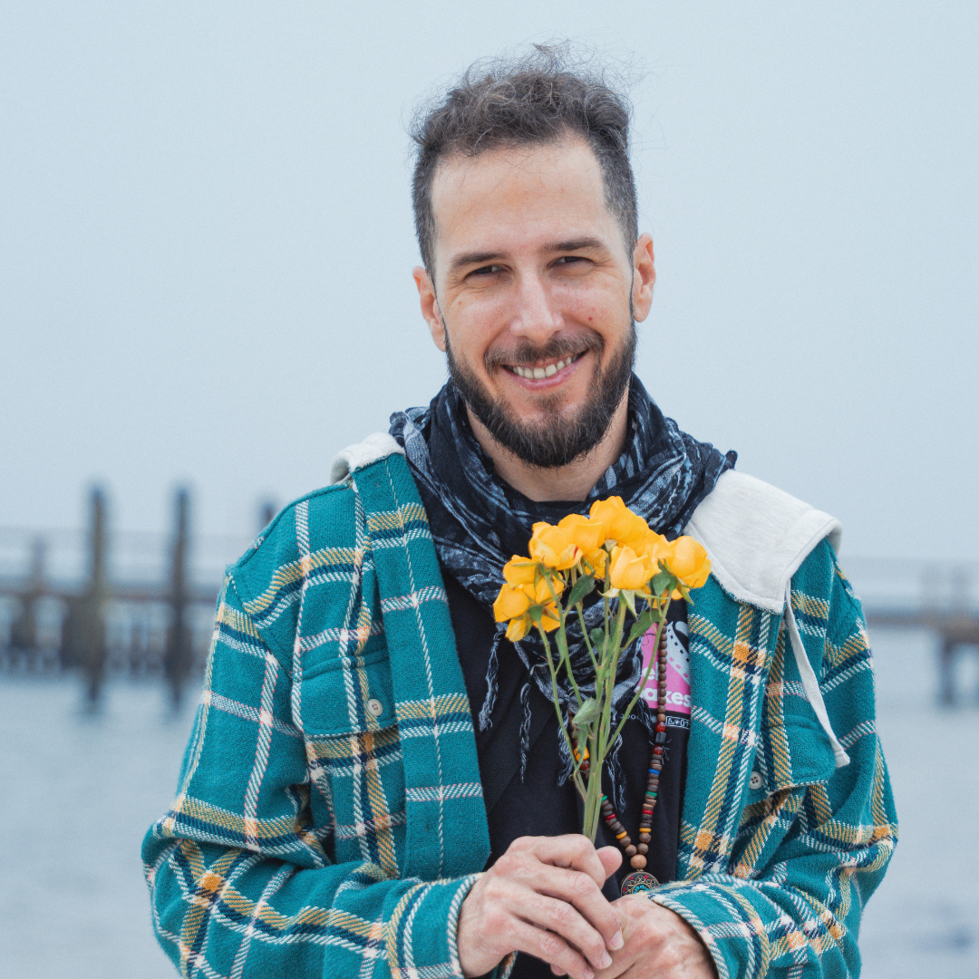 A smiling man holding yellow flowers by the water