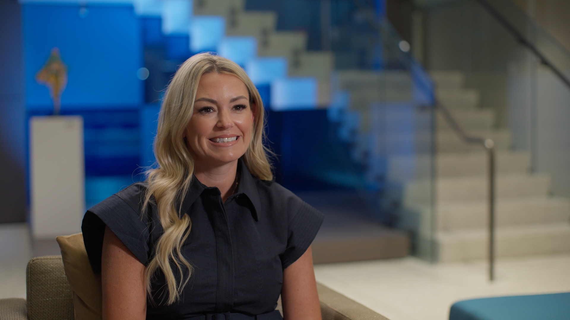 Finished wide interview frame with a warm three-quarter backlight separating the subject from the lobby
