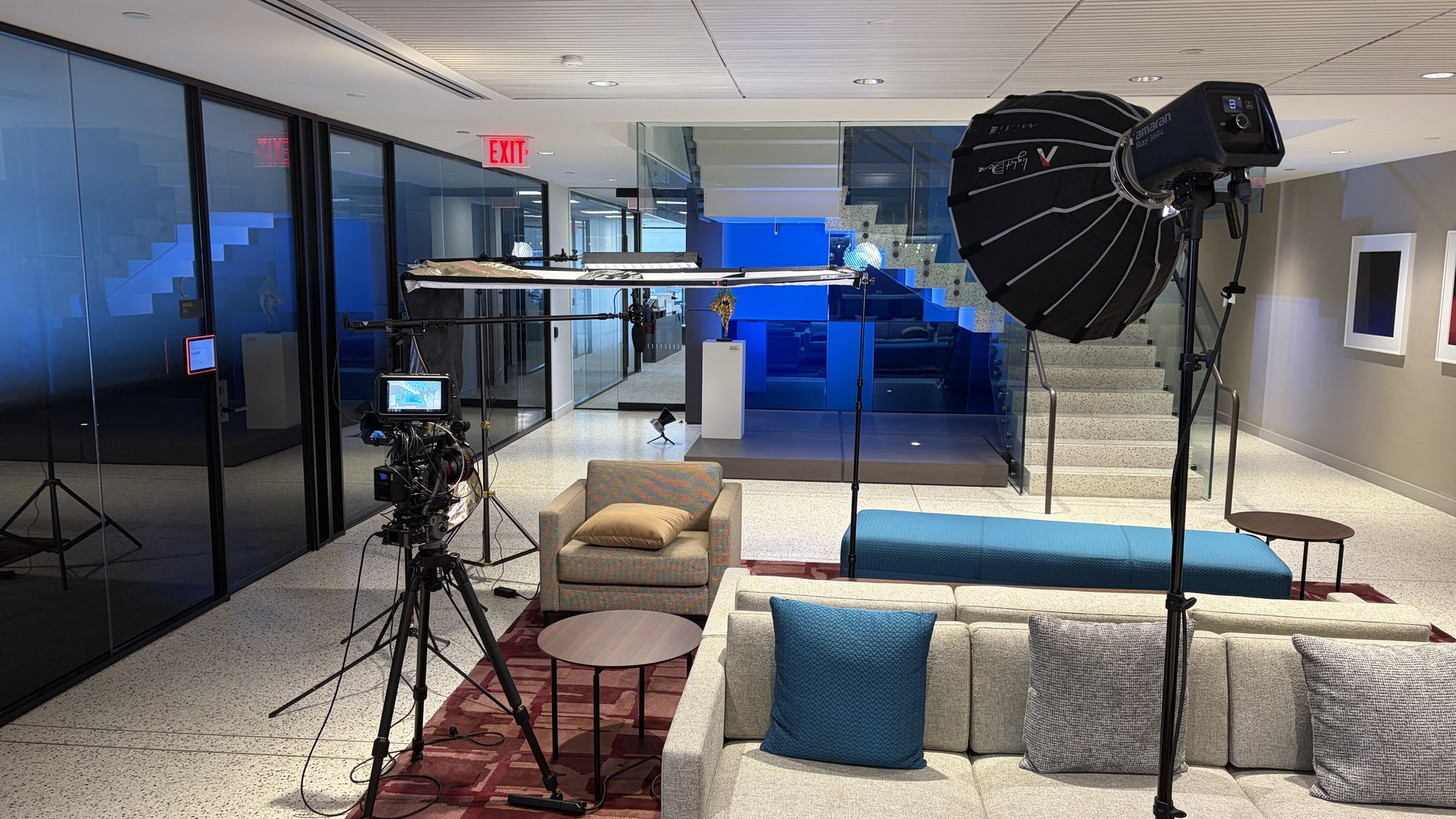 Behind-the-scenes Boston interview setup with camera, overhead diffusion, boom microphone, large soft light, chair, and glass staircase location