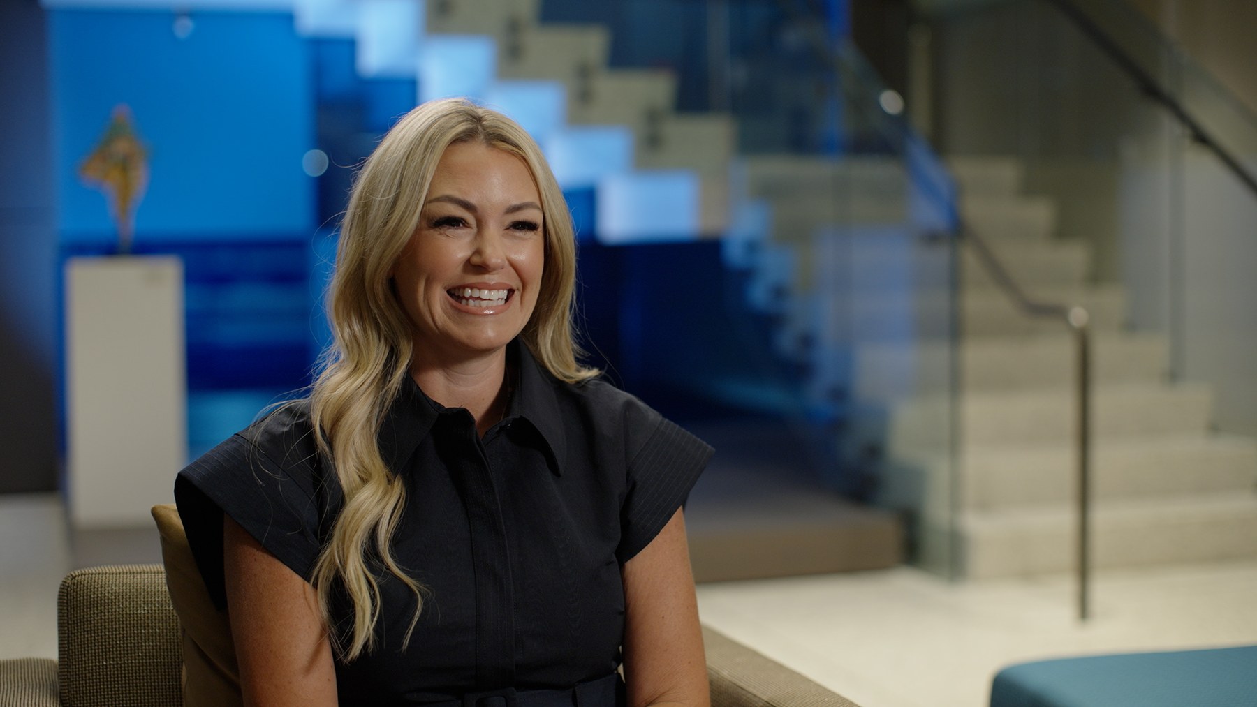 Final Boston interview frame with the subject composed against a blue glass wall and staircase
