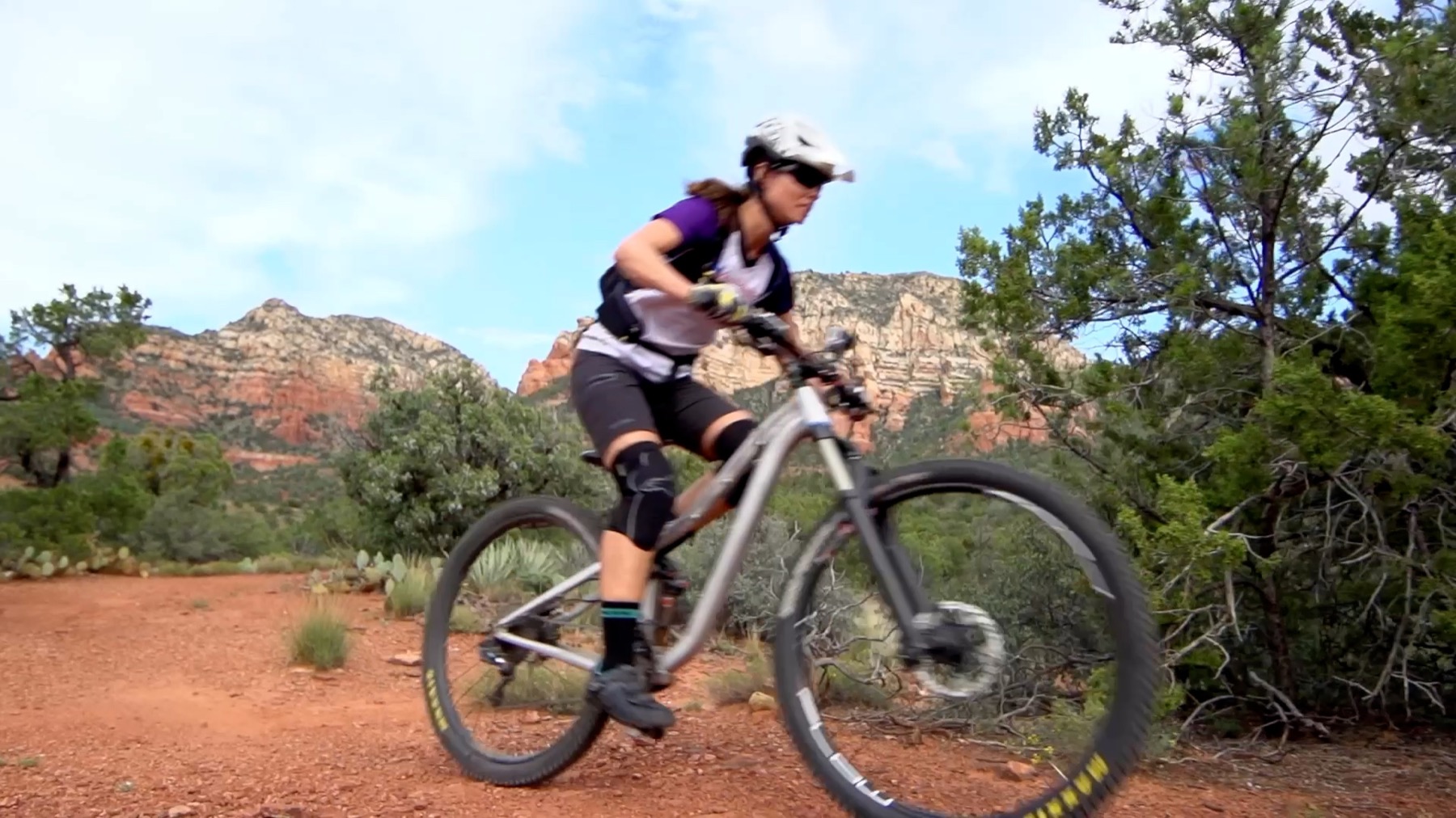Low-angle mountain-bike shot in Sedona with a rider passing close to camera and red-rock mountains framed in the background