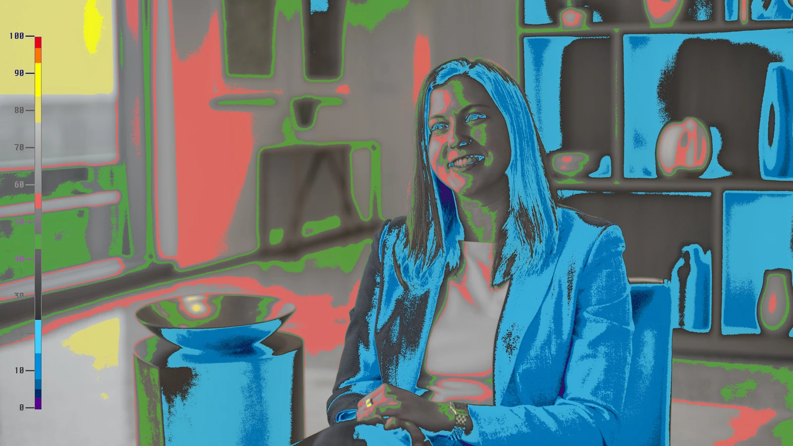 False-color monitor view of the interview subject, bright window, and bookshelf background