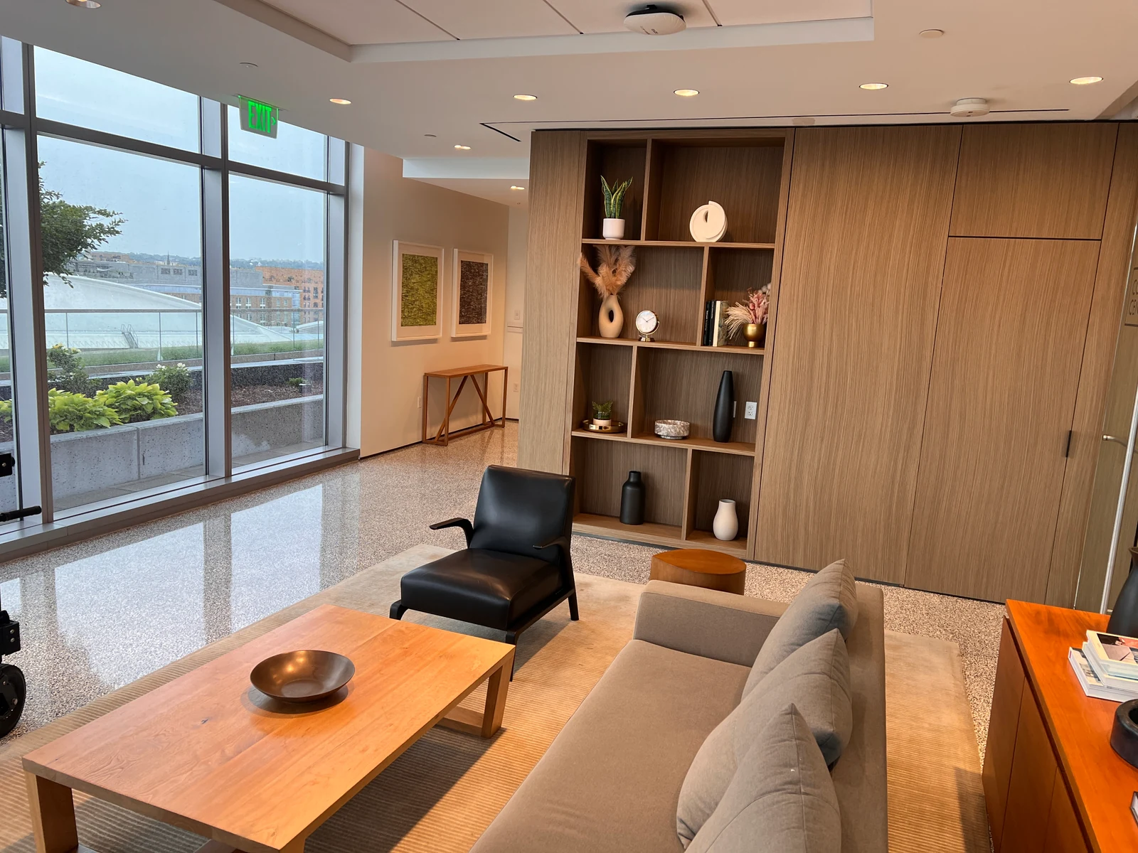 Unlit interview location with large windows, warm ceiling fixtures, bookshelves, and lounge furniture