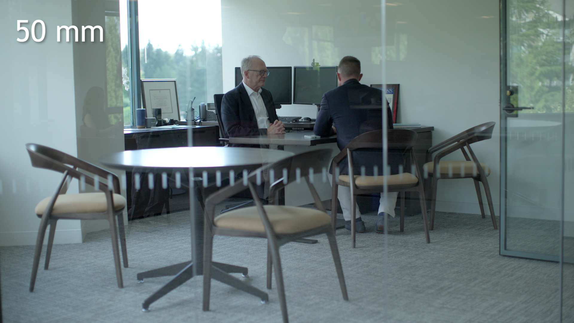 Wide office scene photographed at 50mm from outside the glass-walled room