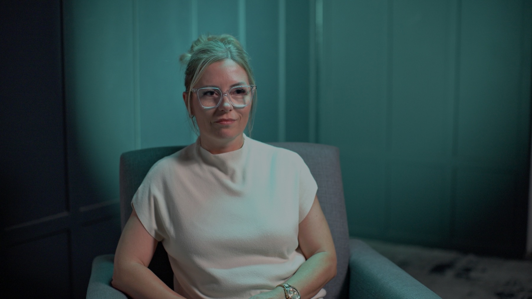 Finished corporate interview frame with a soft key and strong teal RGB edge light on a woman wearing clear glasses and a white shirt