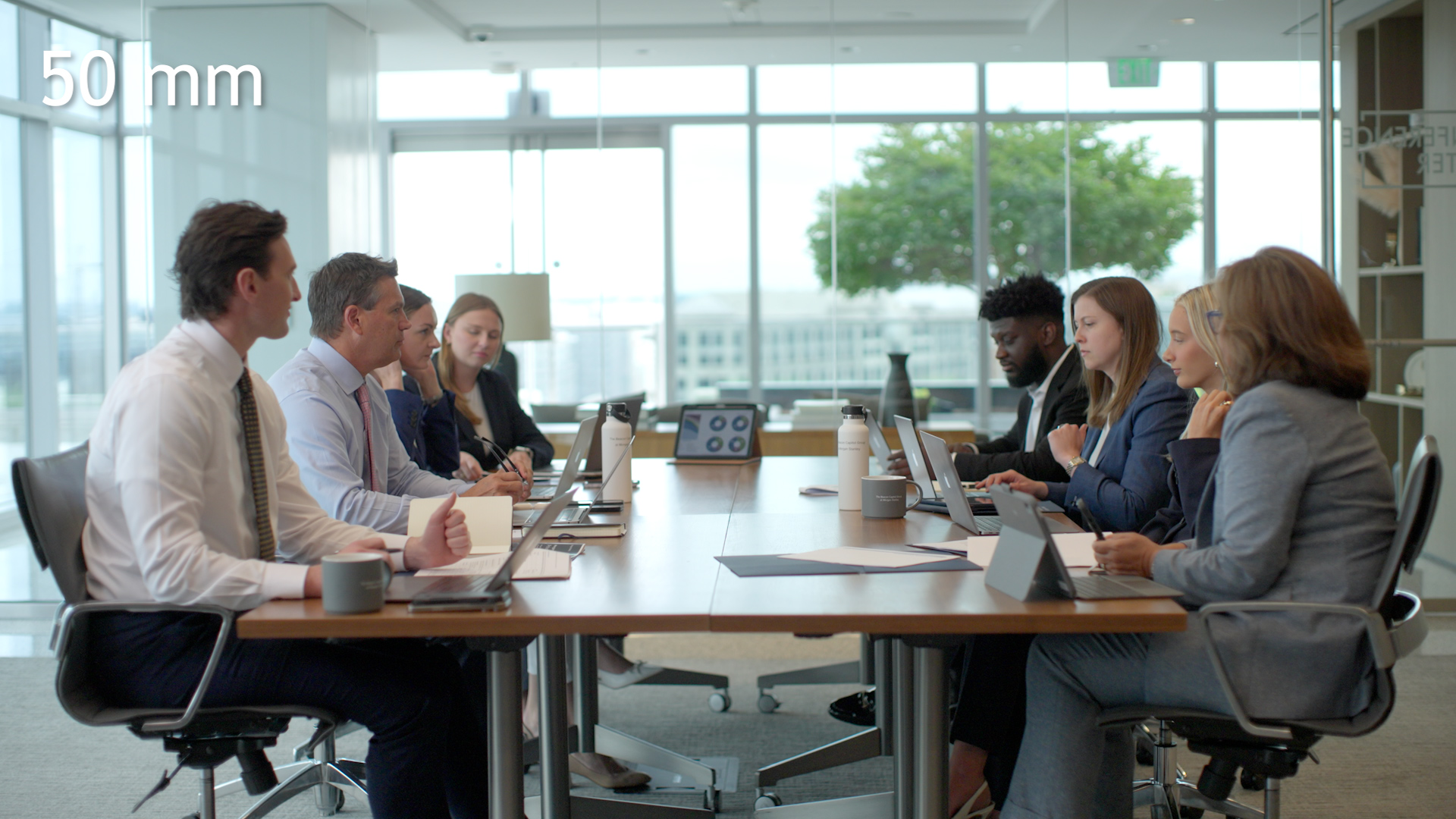 Wide conference-room scene photographed at 50mm with both sides of the table and the room visible