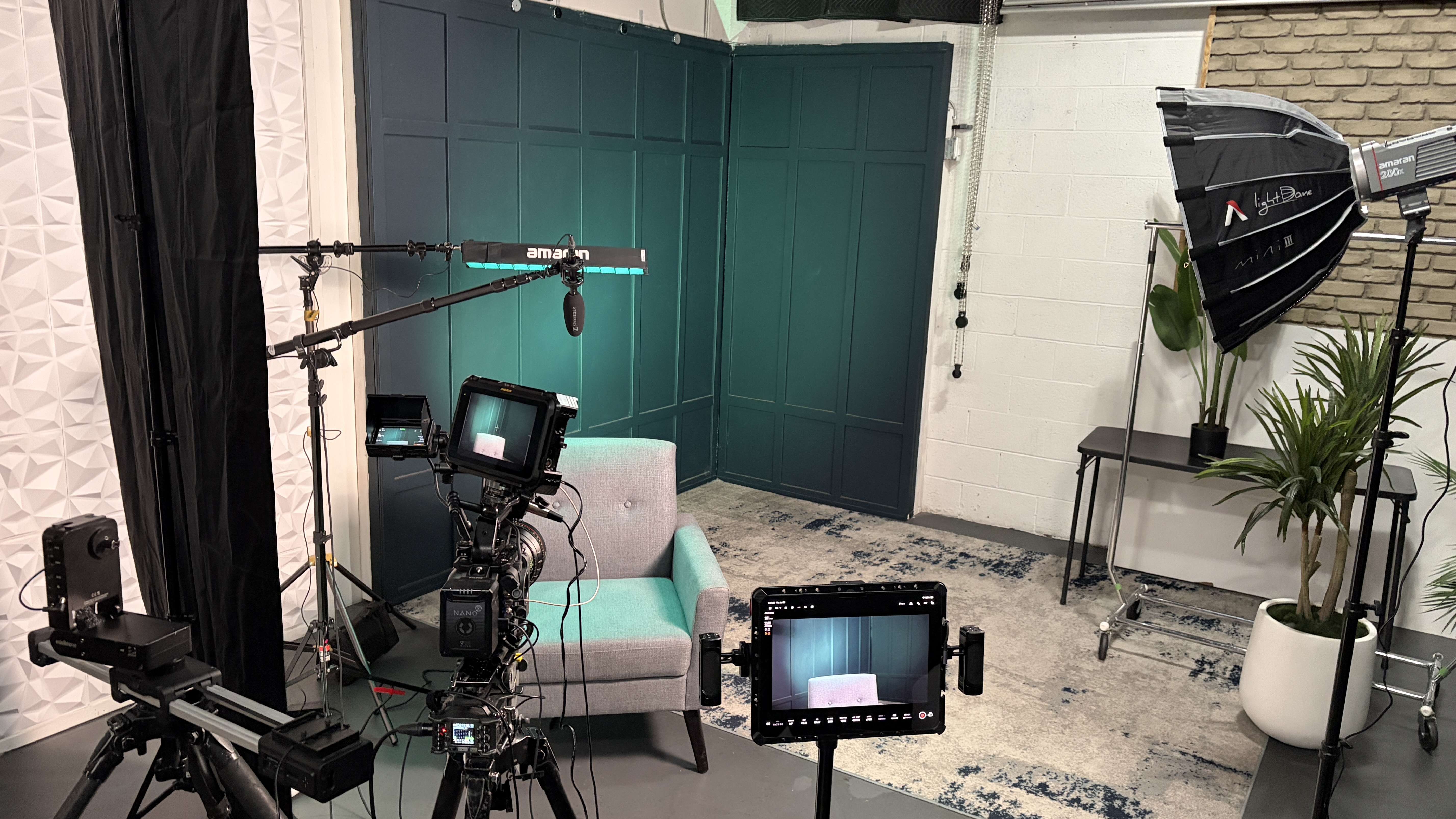 Wide behind-the-scenes view of the corporate interview lighting setup with camera, soft key, RGB tube backlight, and colored background light