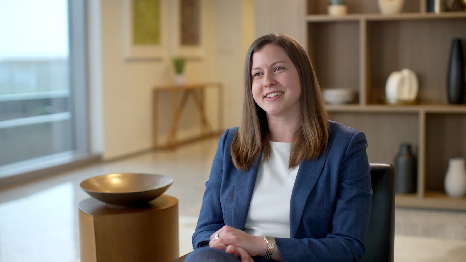 Finished cinematic interview frame of a professional woman seated beside a window and bookshelf