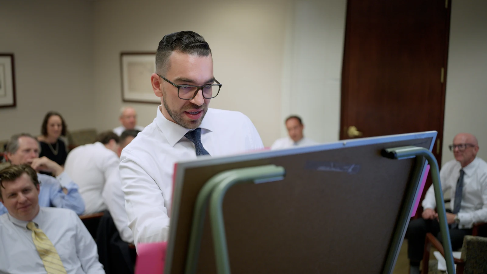 Presenter in a conference room framed with the audience visible behind him