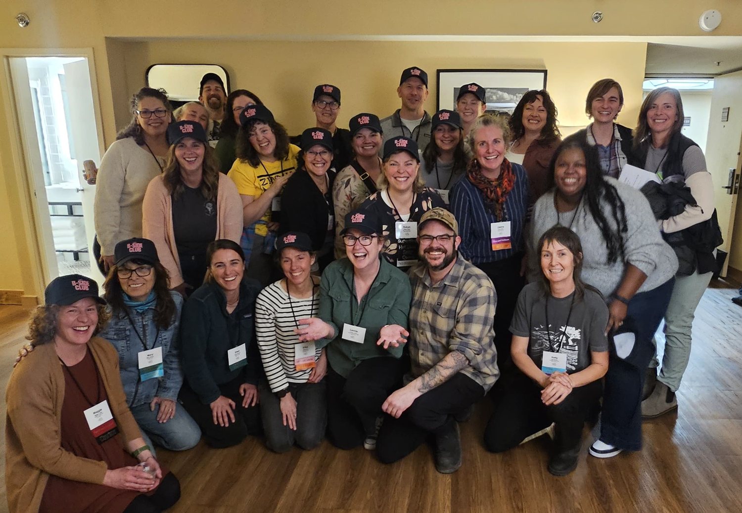 About twenty-five flower farmers and a few partners crowded together for a group photo, many wearing navy B-Side Club caps, all grinning.