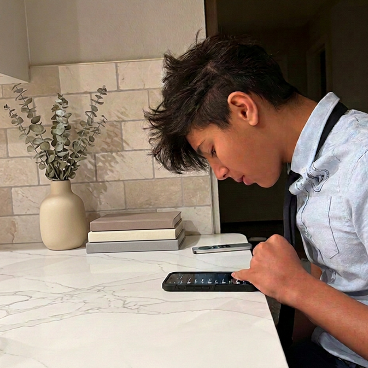 Rayan, 14, head down in his phone at the kitchen counter