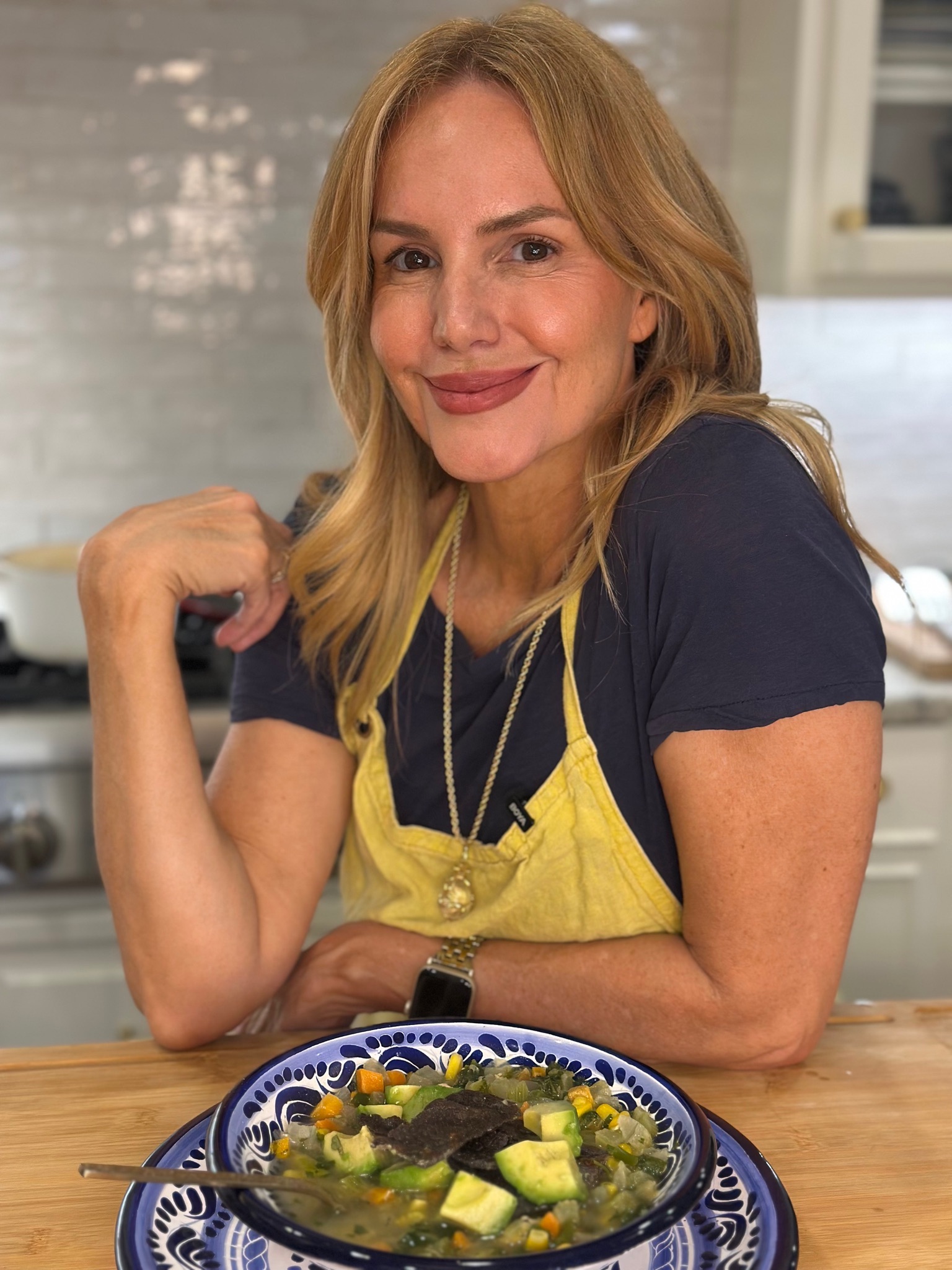 Mee McCormick in a yellow apron at her kitchen table with a bowl of soup