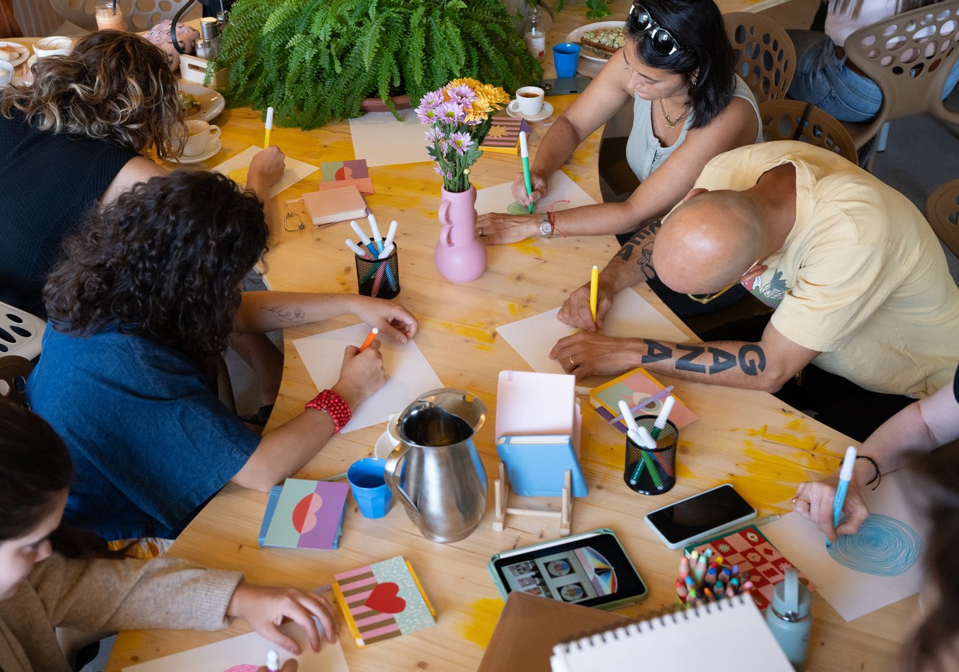 Mujeres creando alrededor de una mesa con libretas de colores