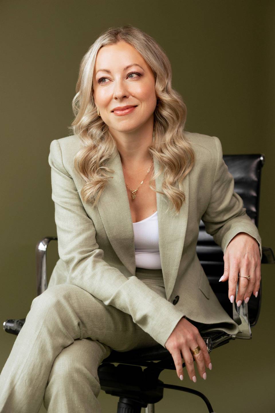 Jess Robertson seated in a sage suit