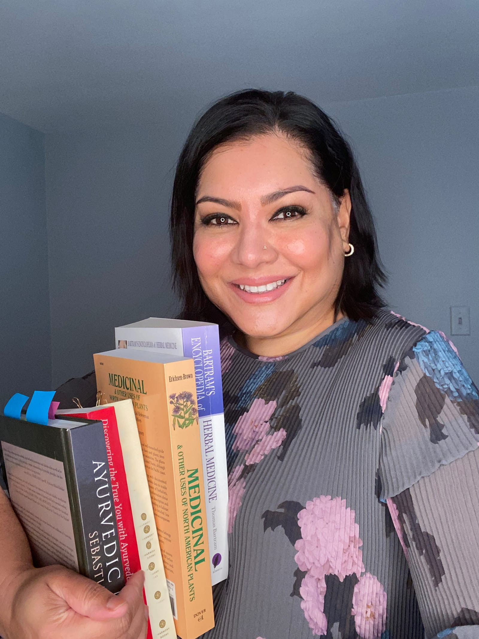 Dr. Arlini Singh holding an armful of Ayurvedic and herbal medicine reference texts.