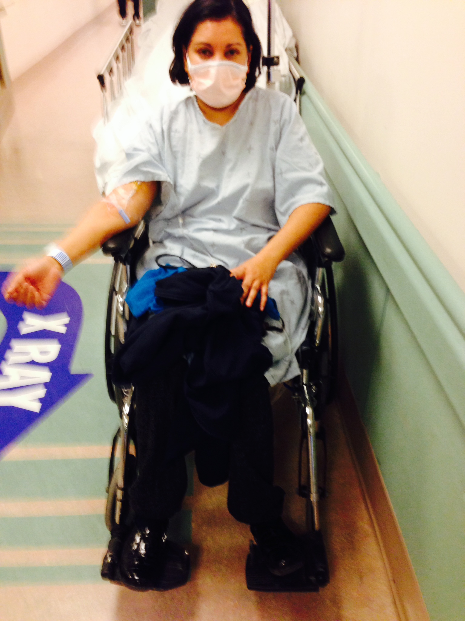 A photograph of Dr. Arlini Singh in the ER, wheelchair-bound, wearing a hospital gown and surgical mask.