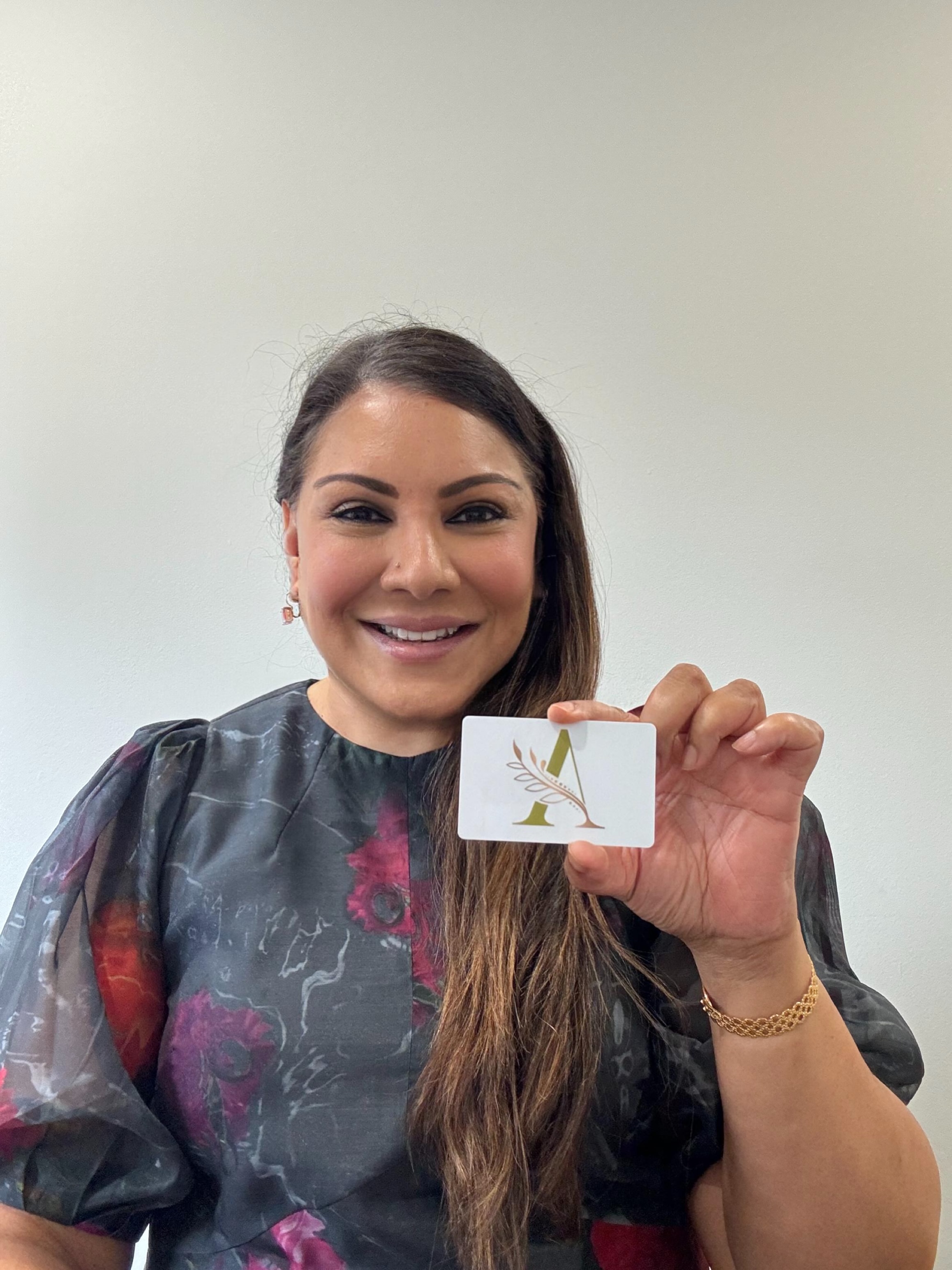 Dr. Arlini Singh holding the A·YUR·VEDA brand card with the gold A and botanical mark.