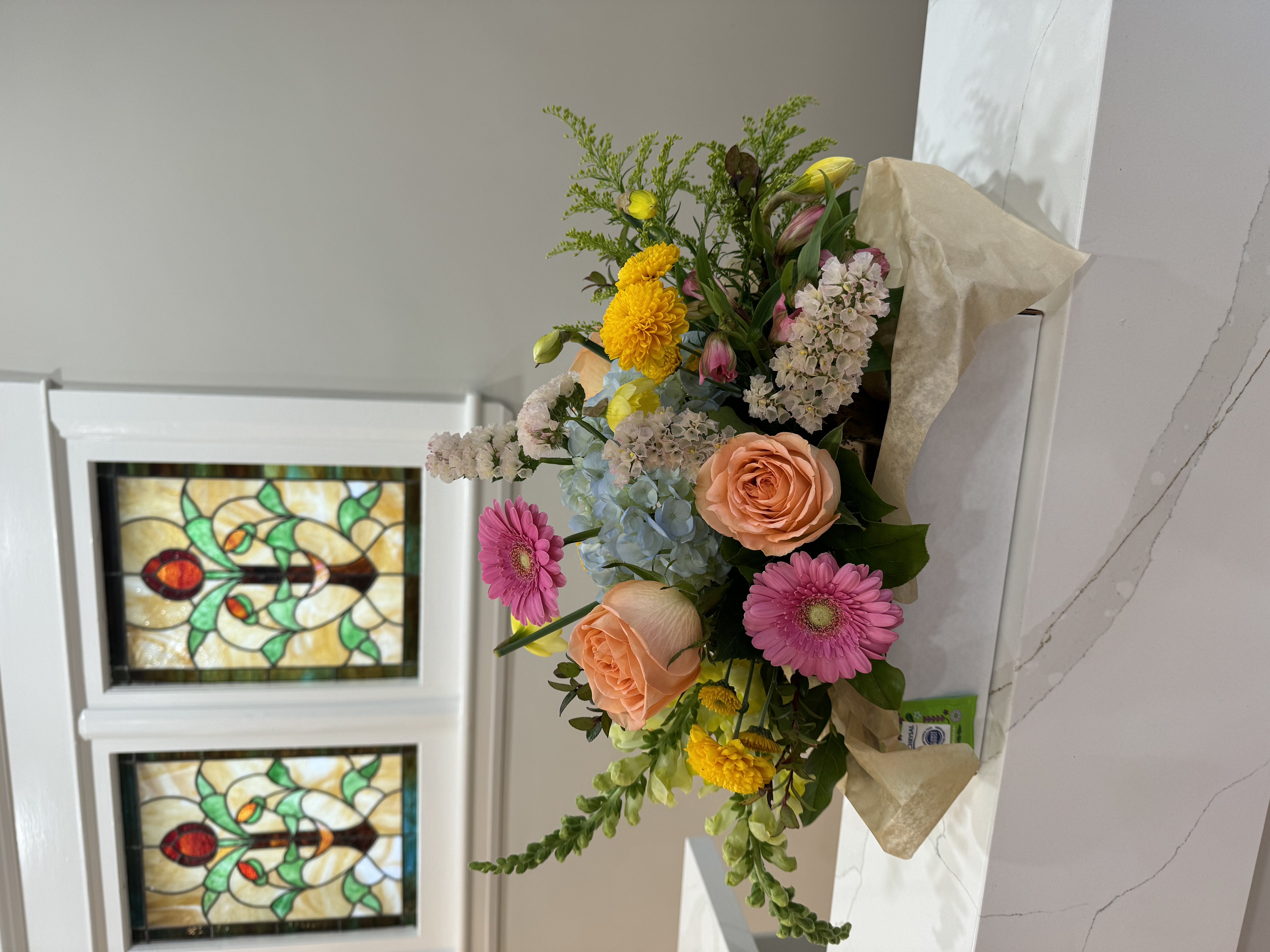 A seasonal flower arrangement on the reception counter at A·YUR·VEDA, beneath the original stained-glass window inside the house.