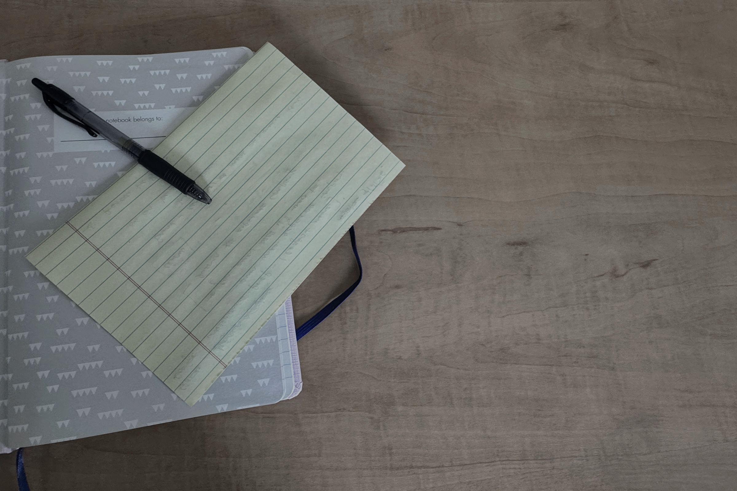 A clinician's open notebook beside a yellow legal pad of handwritten notes and a black pen, on a wooden consultation table, photographed in soft natural light.