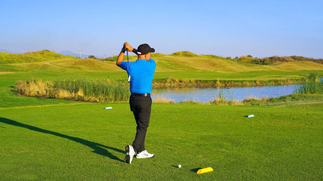 A professional golfer mid-swing, following through a shot on a green links golf course