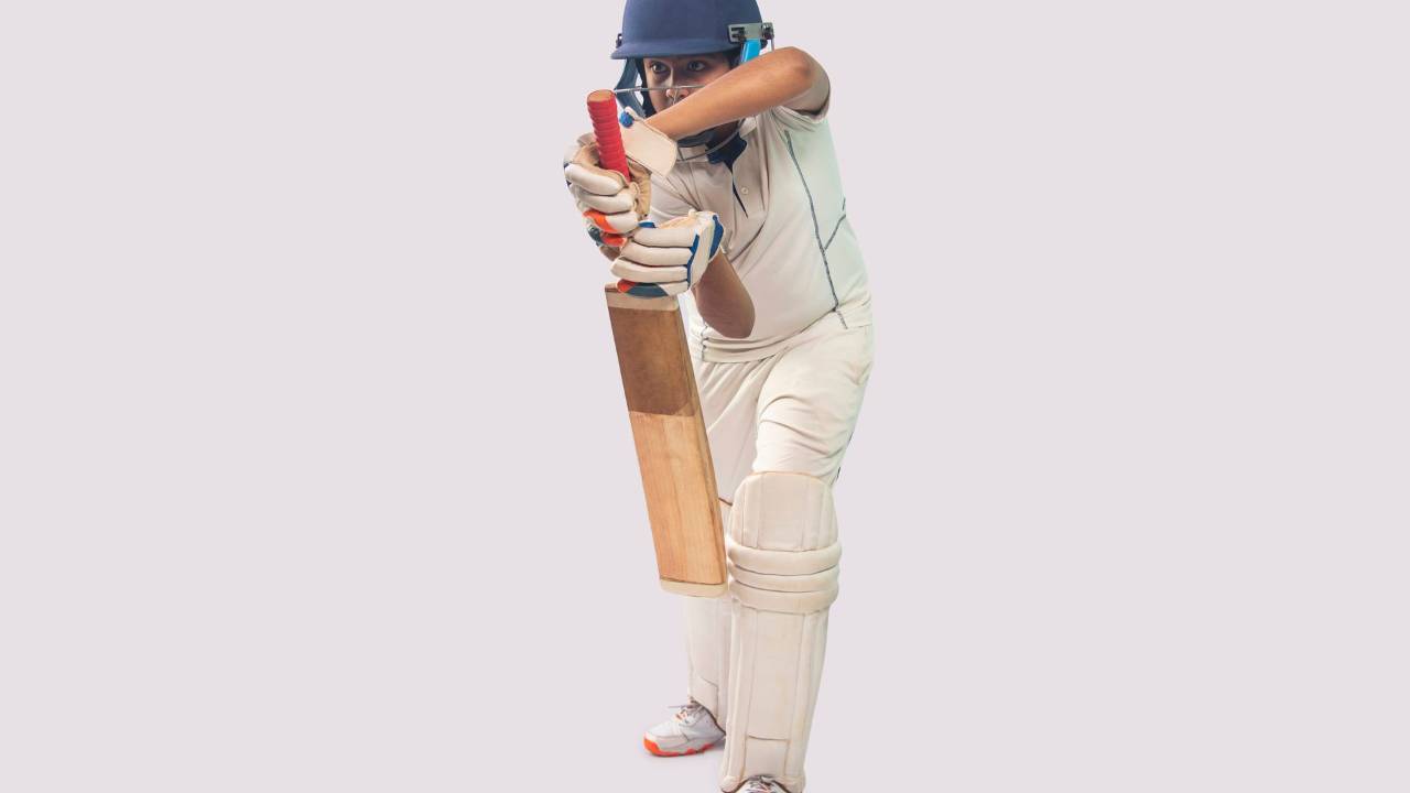 A young cricket player in full whites and pads batting on the pitch