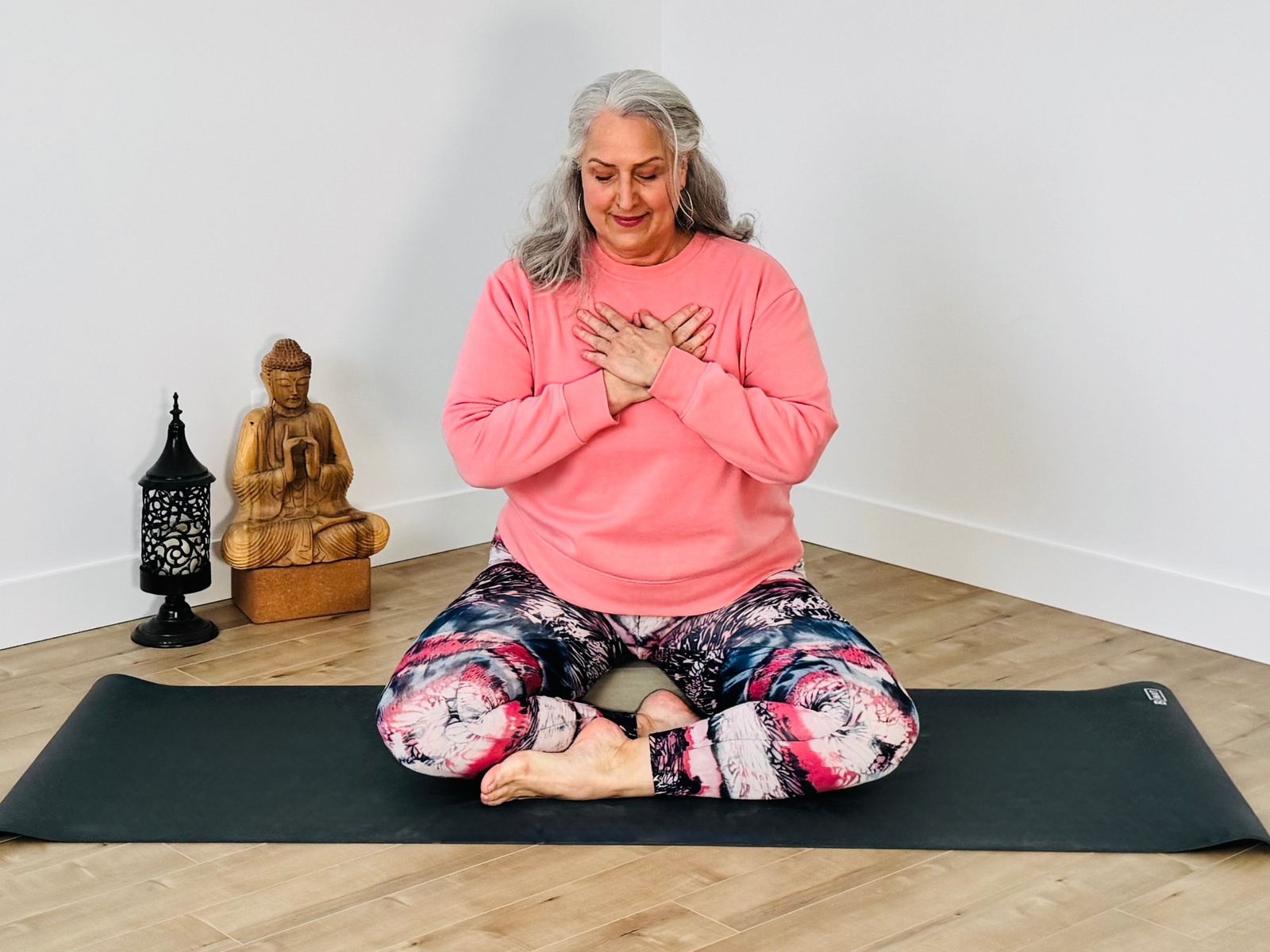 Isabelle Cyr, les mains sur le cœur, assise sur son tapis de yoga