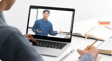 A person takes notes while watching an instructor deliver a live video training on a laptop screen.
