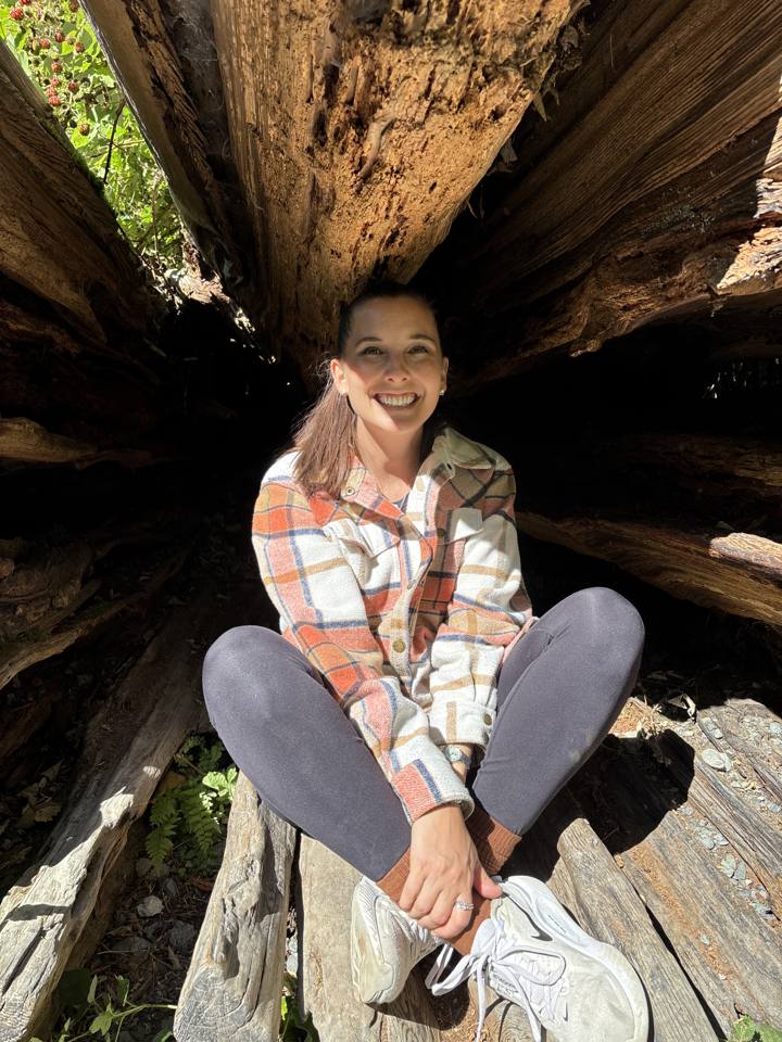 Kierstin smiling, sitting inside a hollow cedar log in the forest