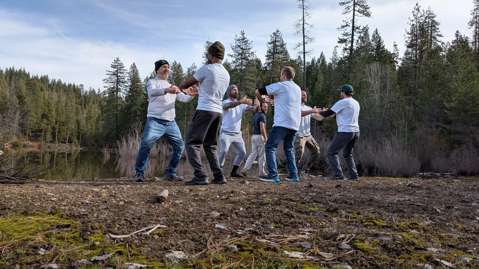 Men practicing embodied movement together beside a forest lake
