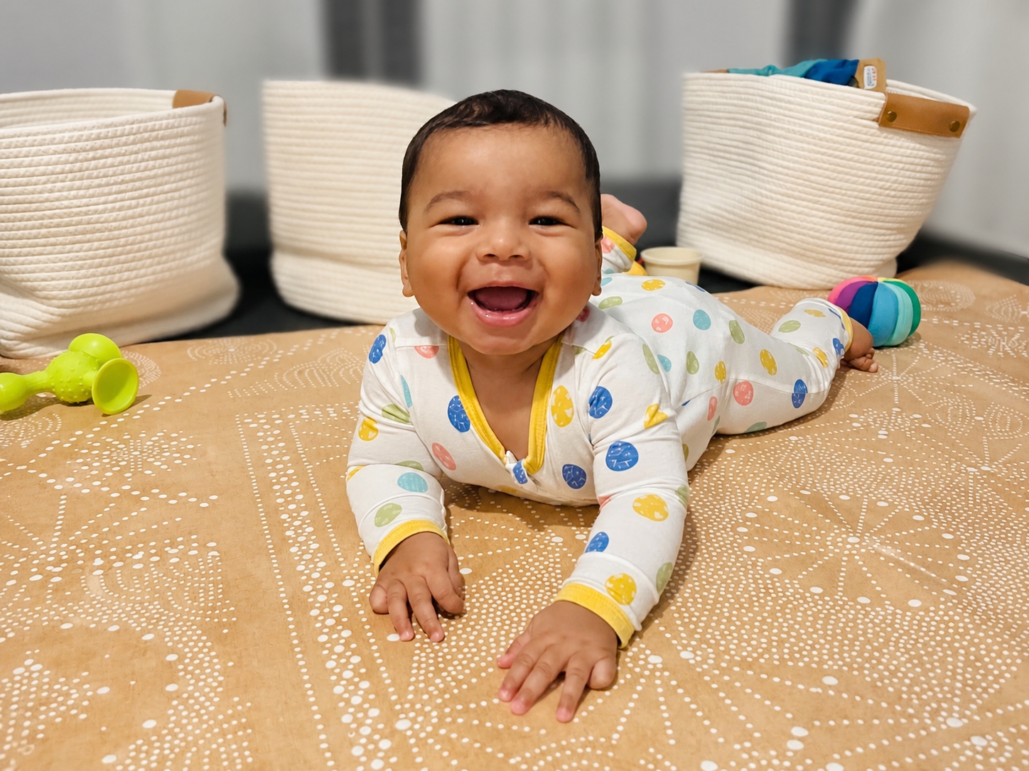 Smiling baby on a patterned play mat with storage baskets behind