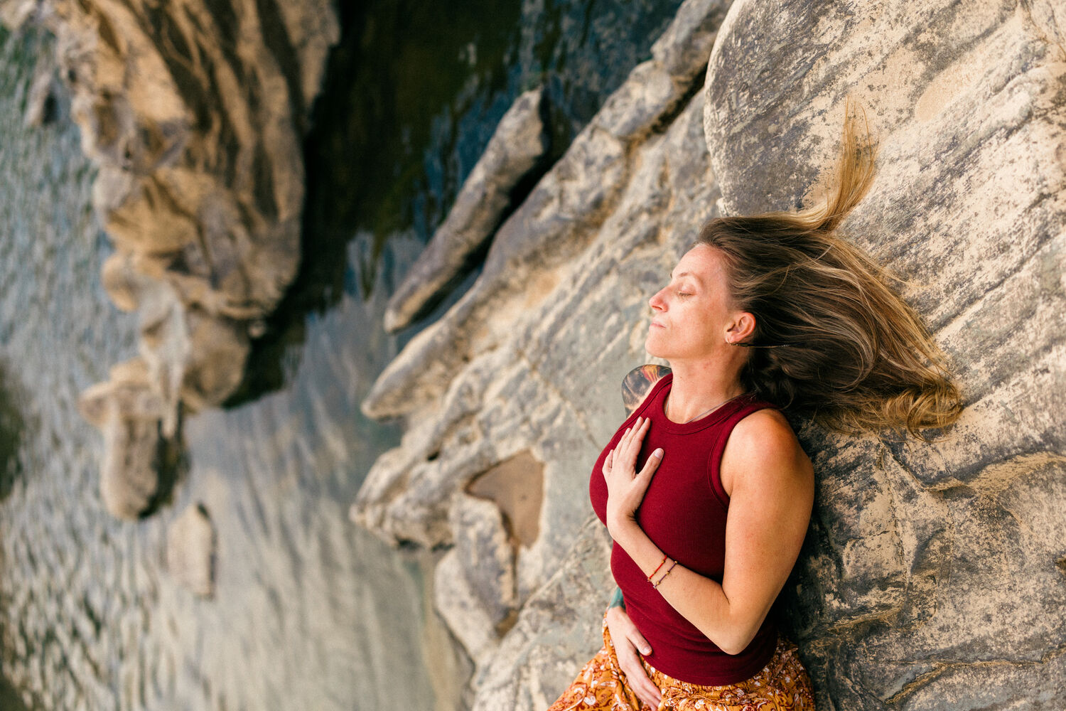 Jean-Marie resting against the rock by the water, hand on her heart