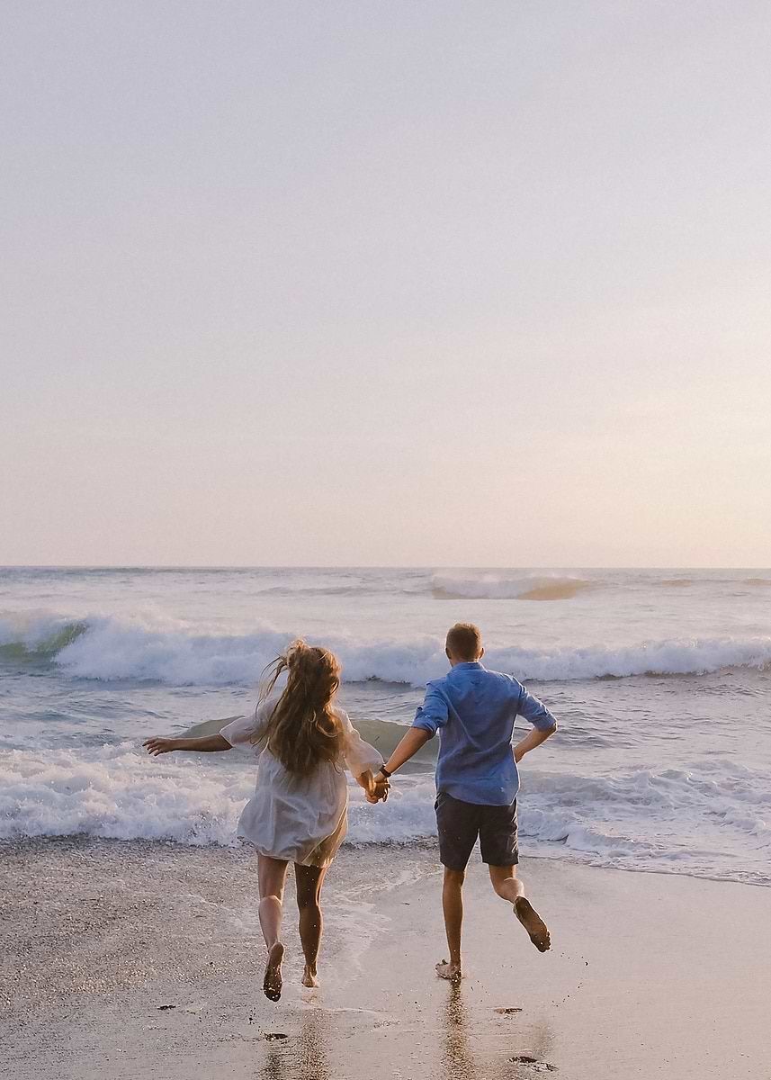 A couple running into the surf together, hand in hand