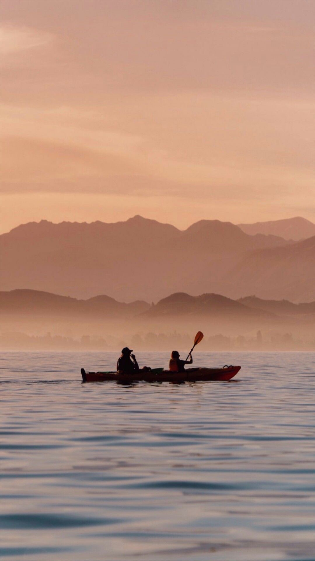Two people paddling one kayak across still water at dusk