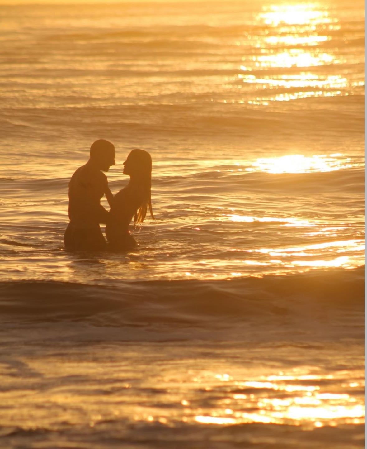 A couple facing each other in the water at sunset