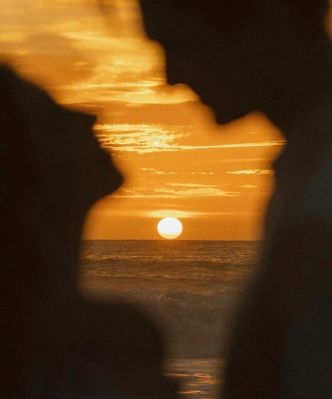 Sunset over the ocean seen between two silhouetted profiles