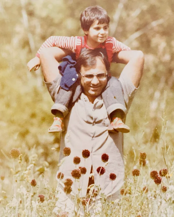 Naz Taylor as a young girl, riding on her father&rsquo;s shoulders in a field of wildflowers.