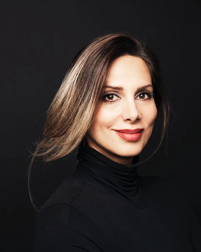 Naz Taylor, journalist and public relations strategist, in a black turtleneck against a near black studio ground.