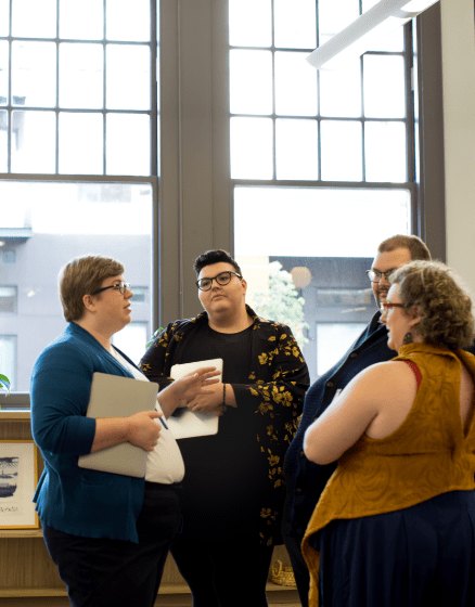 Four colleagues talking together beside a tall studio window