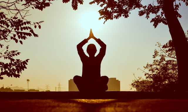 Silhouette practising Yoga at sunrise