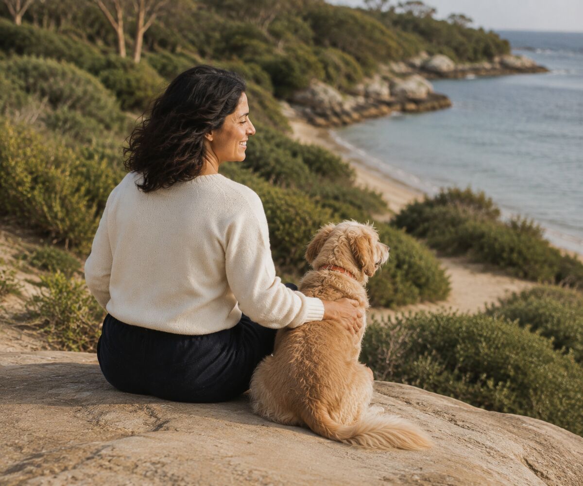A woman sitting beside her dog overlooking the coast